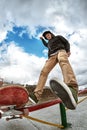 Teen skater in sweatshirt and jeans drops off the railing after sliding on a skateboard in a skate park. Wide angle