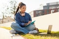 Teen student girl learning outdoors, taking notes while having remote lesson on laptop in university campus park Royalty Free Stock Photo