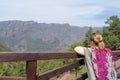 Teen tourist resting, hold a wood fence, relaxing and look the environment national park with colorful dress. Blonde woman observe