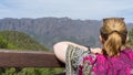 Teen tourist resting, hold a wood fence, relaxing and look the environment national park with colorful dress. Blonde woman observe