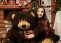 Teenag girl is embraces a big big teddy bear on christmas near fireplace Royalty Free Stock Photo