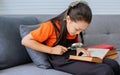 Teenage Asian girl wearing casual clothes, sitting on sofa in cozy indoor living room at home, studying, doing homework, reading Royalty Free Stock Photo