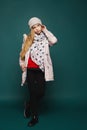 A teenage blonde model girl in modish winter clothes posing over the dark background in full length. Happy girl wearing