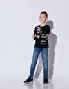 Teenage boy in black jumper and sneakers, blue jeans, bracelet. He standing with folded hands, posing isolated on white background