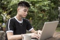 A teenage boy busily types on the laptop for his thesis at a bench by the garden area. Filipino descent