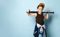 Teenage boy in cap, undershirt, jeans and hoodie tied around his waist. Holding black baseball bat, posing on blue background Royalty Free Stock Photo