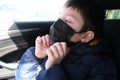 A teenage boy in car putting on surgical medical black face mask as a protection against virus disease, coronavirus covid 19 Royalty Free Stock Photo