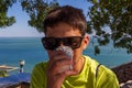 A teenage boy with dark glasses drinks coffee from a disposable Cup against the background of the sea. Royalty Free Stock Photo