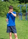 Teenage boy exercising outdoors, sports ground in the yard, he opens a bottle of water and drinks, healthy lifestyle Royalty Free Stock Photo