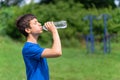 Teenage boy exercising outdoors, sports ground in the yard, he opens a bottle of water and drinks, healthy lifestyle Royalty Free Stock Photo