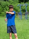 Teenage boy exercising outdoors, sports ground in the yard, he opens a bottle of water and drinks, healthy lifestyle Royalty Free Stock Photo