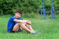 Teenage boy exercising outdoors, sports ground in the yard, he sits on the green grass of the playground, healthy lifestyle Royalty Free Stock Photo