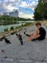 A teenage boy feeds pigeons from his hands on the river bank in the park Royalty Free Stock Photo