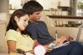 Teenage Boy And Girl Sitting On Sofa At Home Doing Homework Using Laptop Computer Whilst Holding Mobile Phone Royalty Free Stock Photo