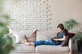 A teenage boy in headphones and with a laptop sits at home on the couch and communicates with peers using wireless Royalty Free Stock Photo