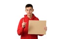 Teenage boy holding blank cardboard banner pointing index finger up. Young guy dressed red hoodie isolated on white