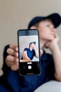 teenage boy holding a smart phone in front of his face at home, taking selfies with his smartphone, digital display on Royalty Free Stock Photo