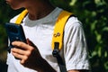 Teenage boy holding smartphone. Kid has yellow backpack with autism infinity rainbow symbol sign. World autism awareness Royalty Free Stock Photo