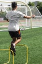 Teenage boy jumping over yellow mini hurdles on a turf field