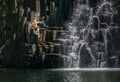 Teenage boy jumping in waterfall lake. Falling water streams flow on black volcanic stone cascades. Rochester Falls waterfall -