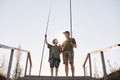 Teenage boy learning to fish with fishing rod, grandpa teaching his grandson to catch fishes, full length portrait on wooden Royalty Free Stock Photo