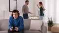 Teenage boy playing videogame while his parents arguing on background. Problems at home Royalty Free Stock Photo