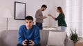 Teenage boy playing videogame while his parents arguing on background. Problems at home Royalty Free Stock Photo