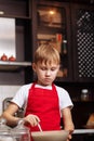 Teenage Boy in red apron in the kitchen at home making dough for pancakes pastry. Children cooking concept