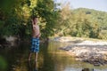 A teenage boy in shorts plays in a mountain river in shallow water