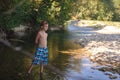 A teenage boy in shorts plays in a mountain river in shallow water