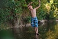 A teenage boy in shorts plays in a mountain river in shallow water