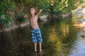 A teenage boy in shorts plays in a mountain river in shallow water