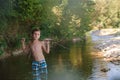 A teenage boy in shorts plays in a mountain river in shallow water