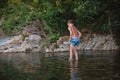 A teenage boy in shorts plays in a mountain river in shallow water