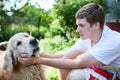 Teenage boy sits down to pat the dog, elderly golden retiever with good young man are in summer garden Royalty Free Stock Photo