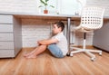 Teenage boy sitting alone and crying under desk in his room at home