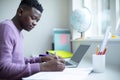 Teenage Boy Sitting At Desk Doing Homework Assignment On Laptop