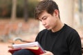 Teenage boy is sitting in a park while doing school homework with a serious face and concentration