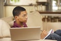 Teenage Boy Sitting On Sofa At Home Doing Homework Using Laptop Computer Whilst Watching TV Royalty Free Stock Photo
