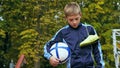 Smiling teenage boy with a soccer ball in his hand and soccer boots on the shoulder against the background of the Royalty Free Stock Photo