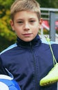 Smiling teenage boy with a soccer ball in his hand and soccer boots on the shoulder against the background of the Royalty Free Stock Photo