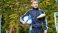 Smiling teenage boy with a soccer ball in his hand and soccer boots on the shoulder against the background of the Royalty Free Stock Photo