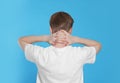 Teenage boy suffering from pain in neck on light blue background, back view. Arthritis symptom Royalty Free Stock Photo