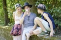 Teenage boy talking into his mobile phone while sitting between brother and mother on a stone wall under trees in a park in summer Royalty Free Stock Photo