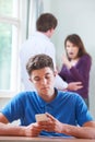 Teenage Boy Texts On Phone As Parents Argue In Background Royalty Free Stock Photo