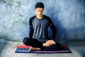 Teenage boy wearing black colored attire and doing yoga on colorful traditional mat and doing Fire Log Pose Agni Stambhasana