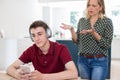 Teenage Boy Wearing Headphones And Using Mobile Phone Being Nagged By Mother At Home Royalty Free Stock Photo