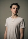 Teenage boy in white T-shirt on gray background. Portrait of confident young man with long hair, eagerness of