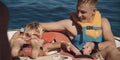 Teenage boy with young boy on holiday sitting on inflatable rib wearing life jackets in the ocean