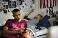 Teenage boys hanging out in a bedroom playing a video game and using a smartphone